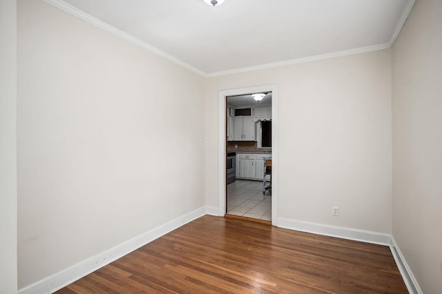 spare room with crown molding, baseboards, and wood finished floors