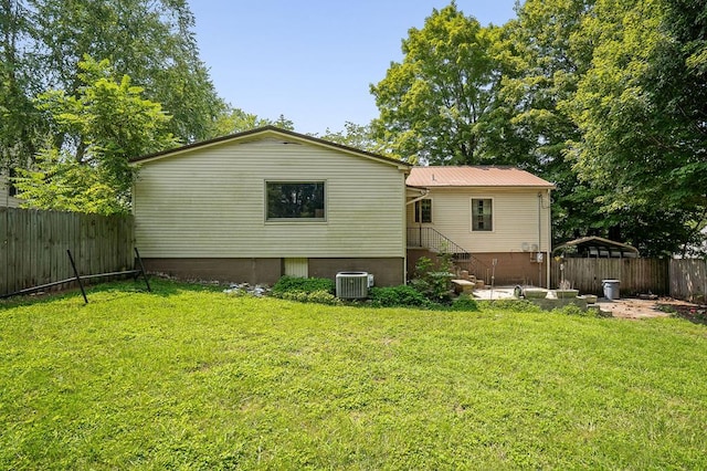 rear view of house with a fenced backyard, central AC, metal roof, and a lawn