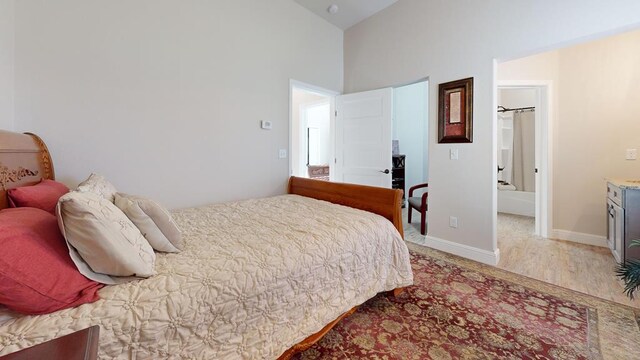 bedroom with high vaulted ceiling, baseboards, and wood finished floors