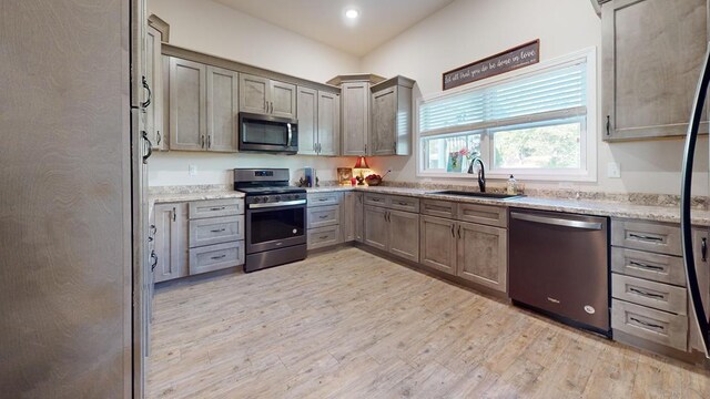 kitchen featuring light wood-style flooring, appliances with stainless steel finishes, light stone countertops, a sink, and recessed lighting