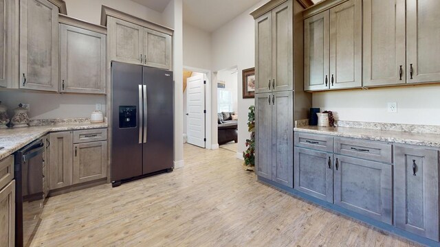 kitchen with light wood-type flooring, black dishwasher, stainless steel fridge, and light stone countertops