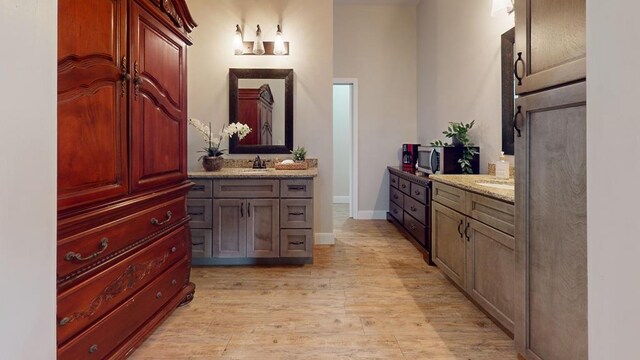 bathroom featuring baseboards, two vanities, a sink, and wood finished floors