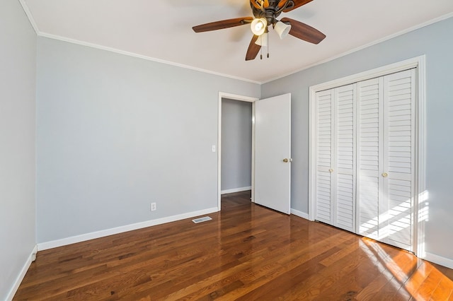 unfurnished bedroom with visible vents, baseboards, a closet, dark wood-style floors, and crown molding