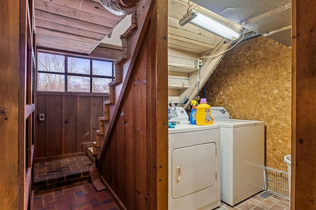 laundry room with laundry area, washer and clothes dryer, brick floor, and wooden walls