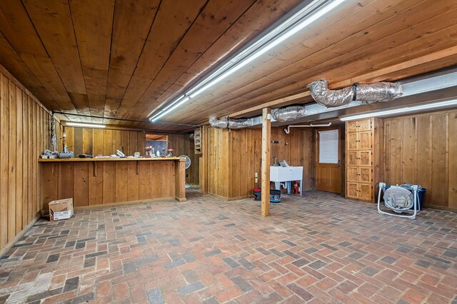 finished basement with brick floor, wooden ceiling, wooden walls, a sink, and a bar