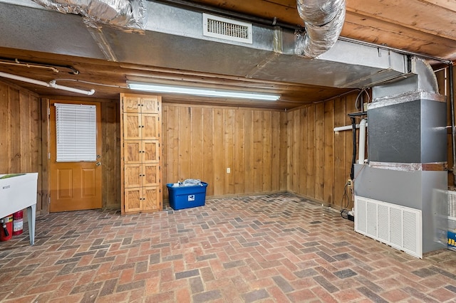 finished below grade area featuring wood walls, brick floor, visible vents, and heating unit