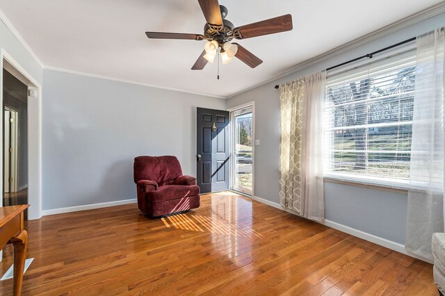 living area with ornamental molding, a ceiling fan, baseboards, and wood finished floors