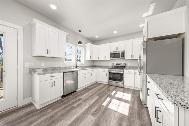 kitchen with stainless steel appliances, hanging light fixtures, a sink, and white cabinetry