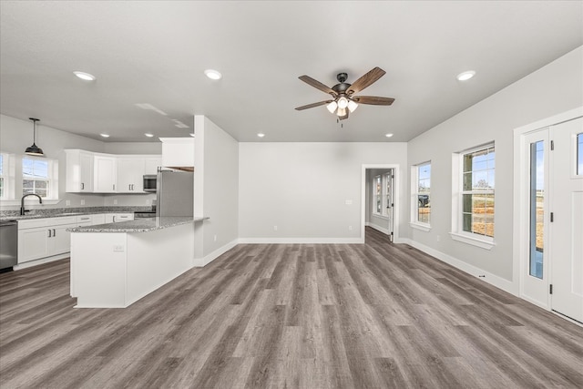 kitchen with light stone counters, appliances with stainless steel finishes, light wood-style floors, open floor plan, and white cabinetry