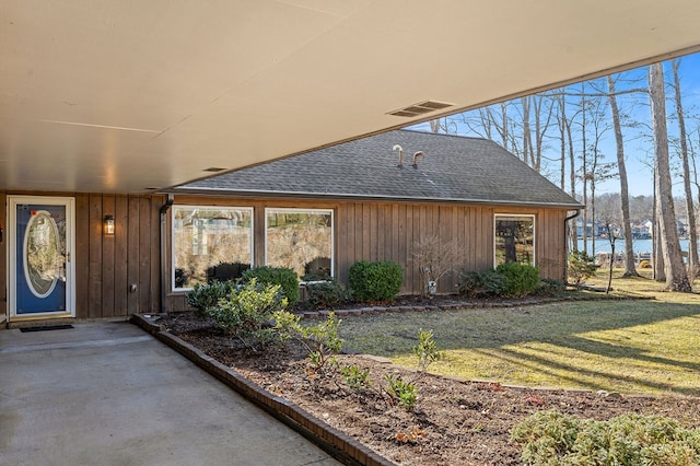 property entrance with roof with shingles, a lawn, and visible vents