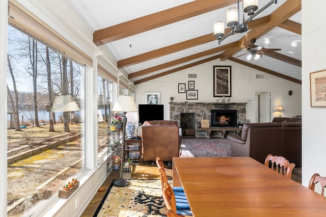 dining area featuring visible vents, a water view, lofted ceiling with beams, ceiling fan, and a stone fireplace