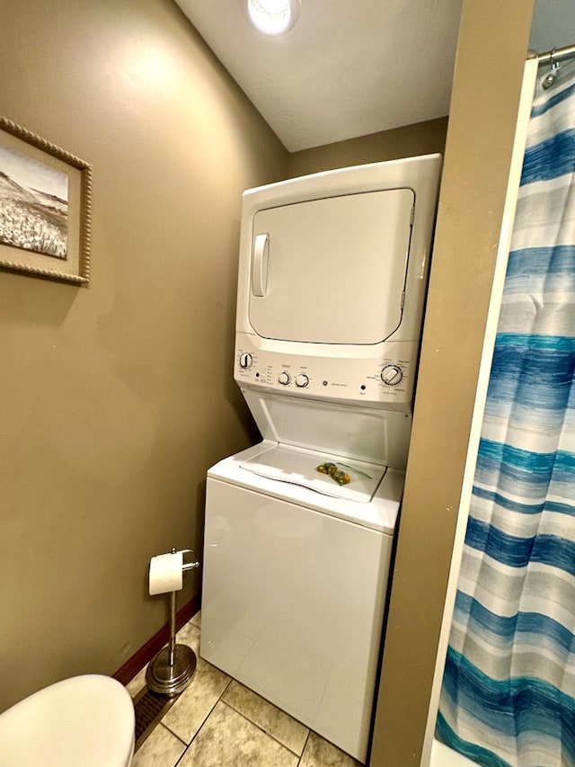 clothes washing area with stacked washer and dryer, laundry area, light tile patterned flooring, and baseboards