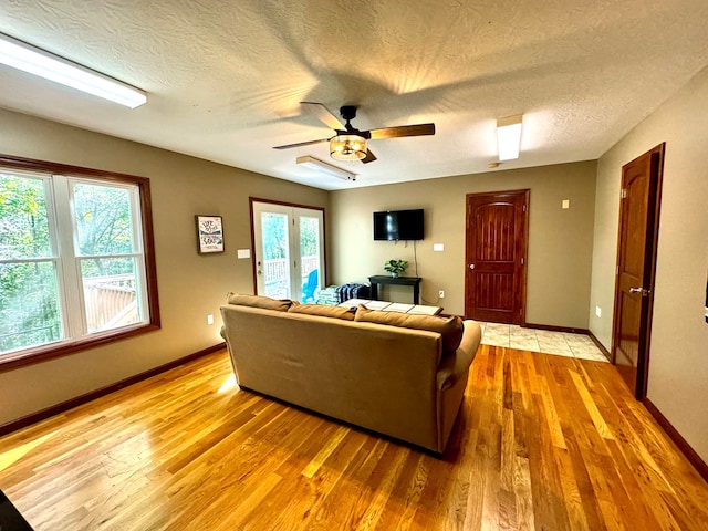 living room with a ceiling fan, baseboards, and light wood finished floors