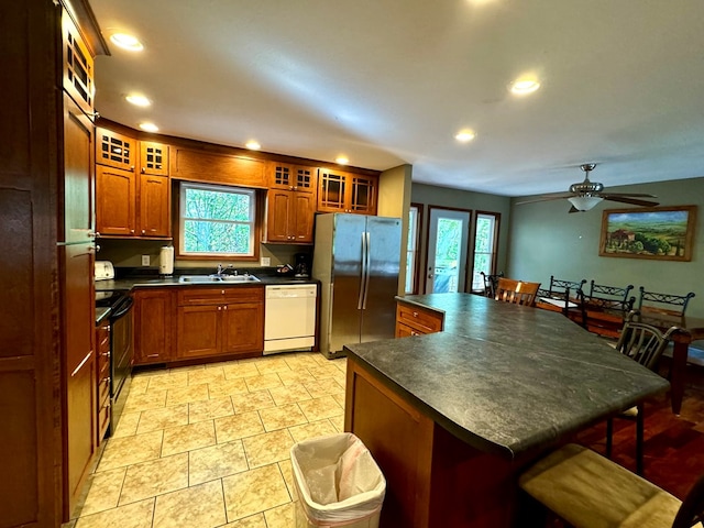 kitchen featuring dark countertops, glass insert cabinets, freestanding refrigerator, white dishwasher, and a sink