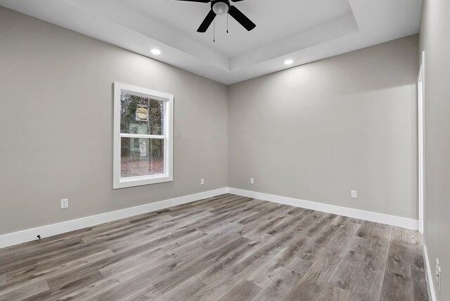 empty room featuring a tray ceiling, baseboards, and light wood finished floors