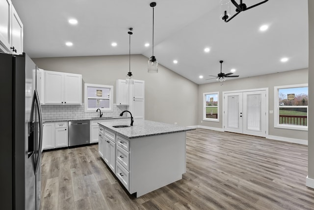 kitchen featuring decorative light fixtures, light stone countertops, a kitchen island with sink, stainless steel appliances, and white cabinetry