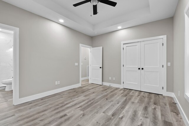 unfurnished bedroom with ensuite bathroom, recessed lighting, light wood-style floors, baseboards, and a tray ceiling