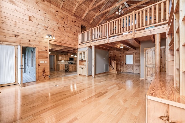 unfurnished living room featuring wooden walls, stairs, high vaulted ceiling, and wood finished floors