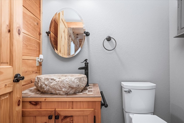 bathroom featuring toilet, a textured wall, and vanity