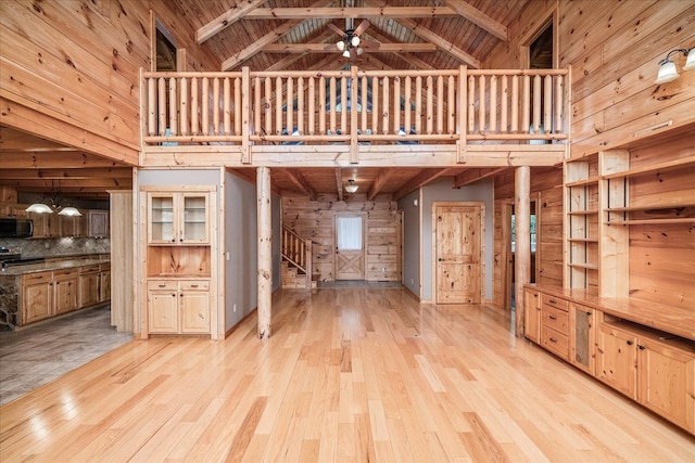 unfurnished living room with high vaulted ceiling, light wood-type flooring, wood ceiling, and wood walls