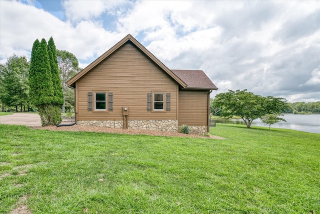 view of side of home featuring a water view, a lawn, and roof with shingles