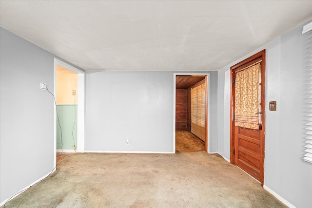 empty room featuring light carpet, a textured ceiling, and baseboards