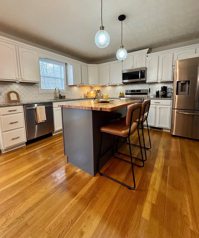 kitchen featuring a center island, decorative light fixtures, stainless steel appliances, butcher block counters, and white cabinetry