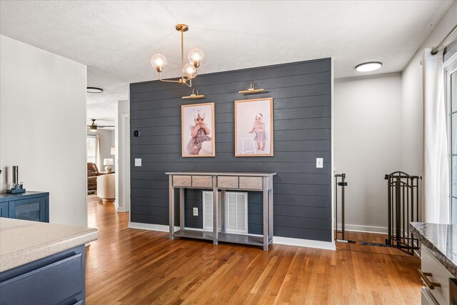 unfurnished living room with ceiling fan with notable chandelier, wood walls, wood finished floors, and baseboards