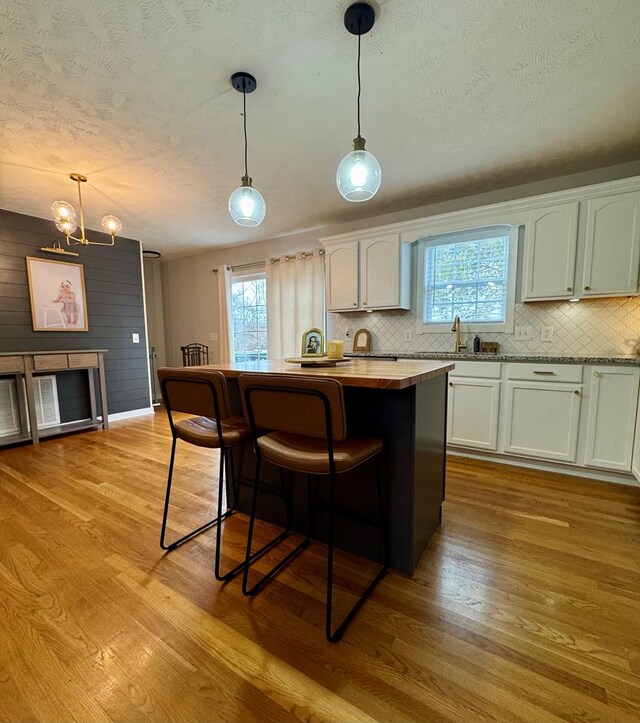 kitchen with light wood finished floors, a kitchen island, white cabinetry, and decorative light fixtures