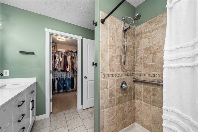 full bath featuring a walk in closet, vanity, a textured ceiling, tile patterned flooring, and tiled shower