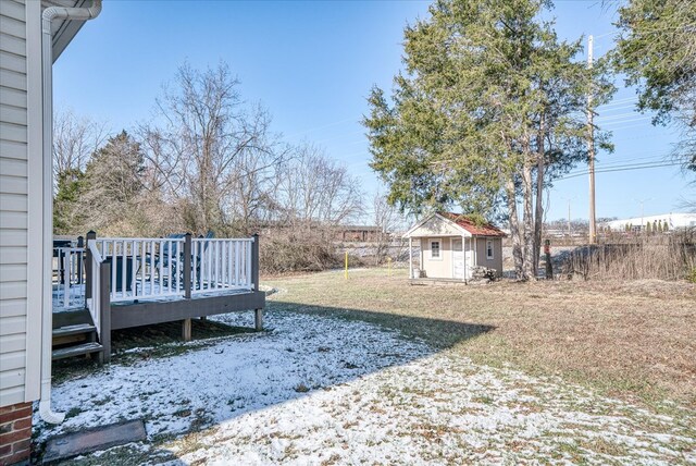 snowy yard with fence, a storage unit, a deck, and an outbuilding