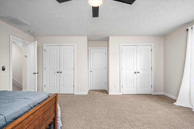 carpeted bedroom featuring visible vents, a textured ceiling, baseboards, and two closets