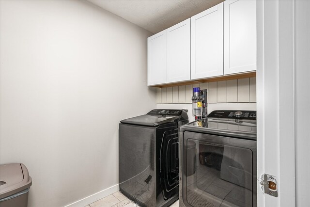 clothes washing area with cabinet space, light tile patterned flooring, a textured ceiling, washer and dryer, and baseboards