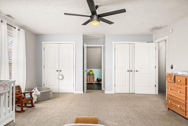 bedroom featuring carpet floors, two closets, visible vents, a ceiling fan, and a textured ceiling