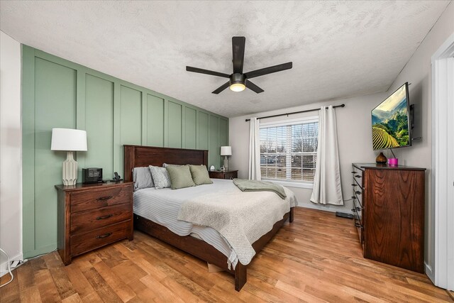 bedroom featuring ceiling fan, a textured ceiling, a decorative wall, and wood finished floors