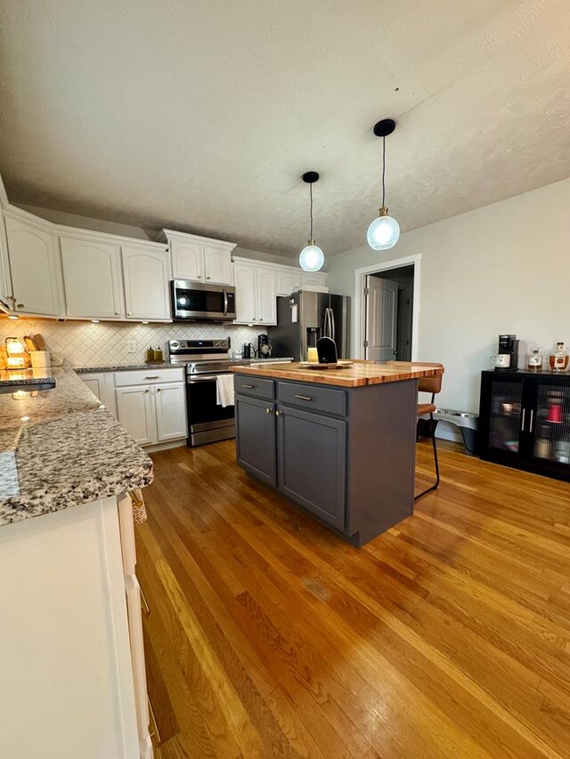 kitchen featuring stainless steel appliances, butcher block counters, white cabinets, gray cabinets, and pendant lighting