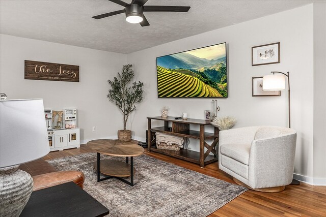 living area featuring a textured ceiling, ceiling fan, wood finished floors, and baseboards