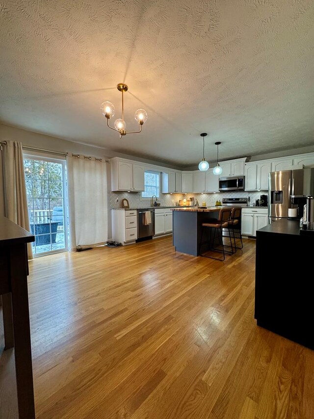 kitchen featuring appliances with stainless steel finishes, a kitchen breakfast bar, a center island, hanging light fixtures, and white cabinetry