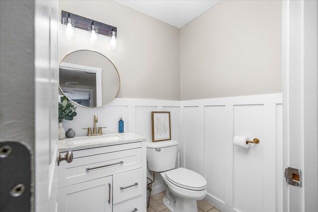 bathroom featuring toilet, a wainscoted wall, tile patterned flooring, vanity, and a decorative wall