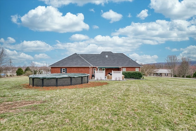 back of property with brick siding, a covered pool, and a yard