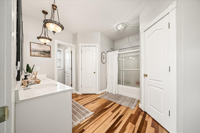 bathroom featuring wood finished floors, a sink, baseboards, double vanity, and shower / bathtub combination with curtain