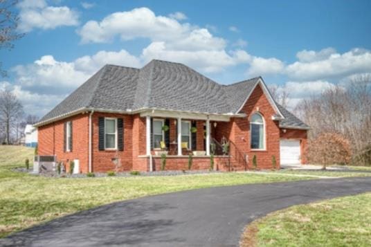 view of front of house featuring brick siding, central AC unit, aphalt driveway, and a front yard