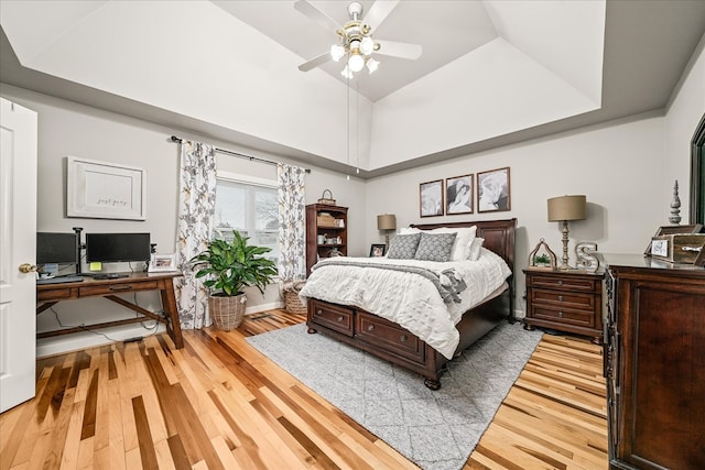 bedroom featuring lofted ceiling, light wood finished floors, a raised ceiling, and a ceiling fan