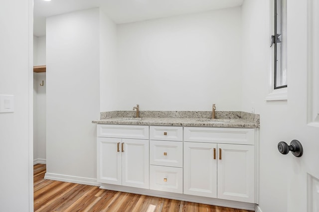 bathroom featuring double vanity, wood finished floors, baseboards, and a sink