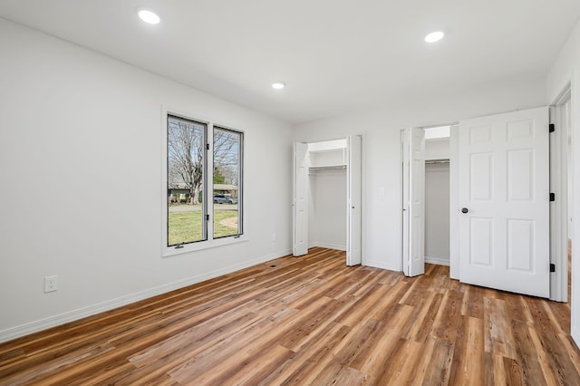 unfurnished bedroom with recessed lighting, light wood-style flooring, baseboards, and multiple closets