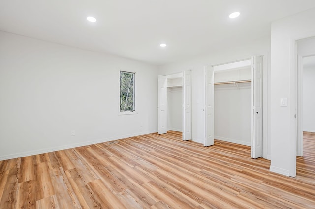 unfurnished bedroom with recessed lighting, light wood-type flooring, baseboards, and two closets