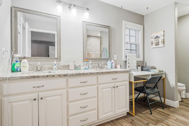 full bath with double vanity, baseboards, toilet, wood finished floors, and a sink