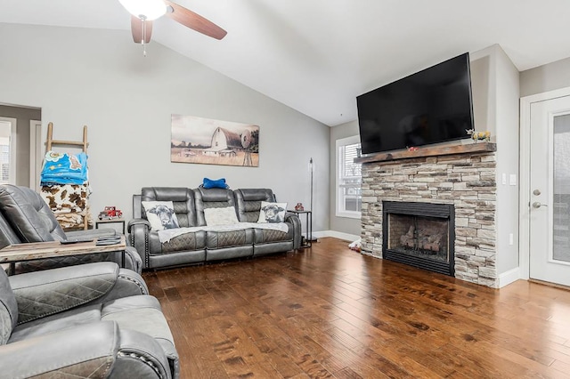 living room featuring vaulted ceiling, a stone fireplace, dark wood finished floors, and baseboards