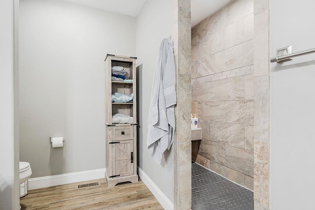 bathroom featuring visible vents, toilet, wood finished floors, baseboards, and walk in shower