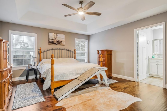 bedroom with dark wood-style floors, a tray ceiling, and baseboards